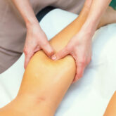 Sports massage therapist performing manual massage therapy technique on the calf muscle of a client